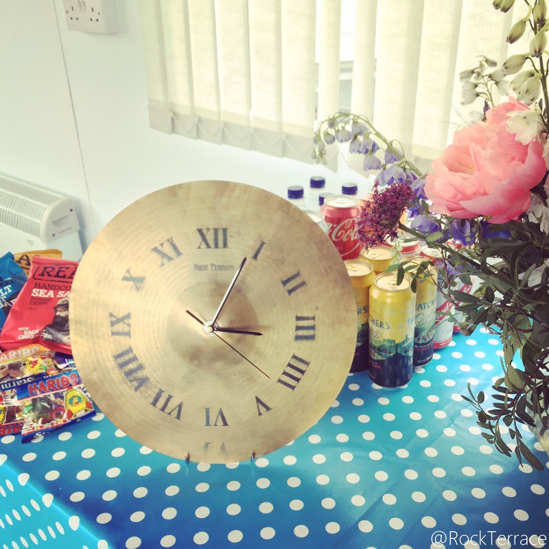 A rock terrace upcycled cymbal clock with flowers and sweets on a blue tablecloth